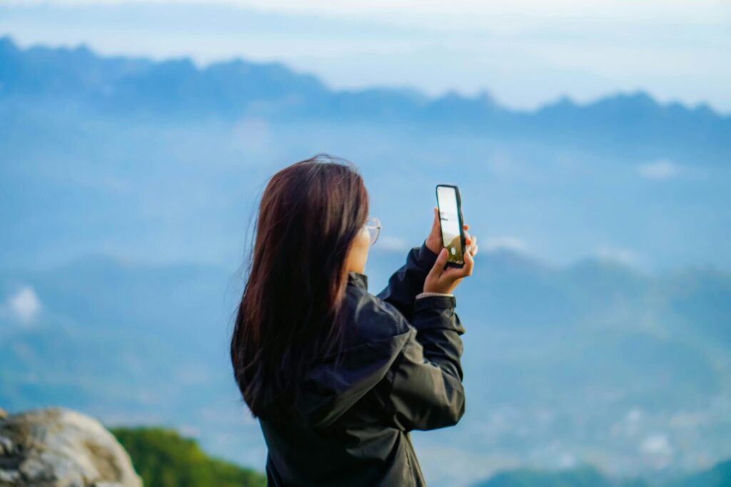 高台から風景をスマホで撮影するメガネの女性