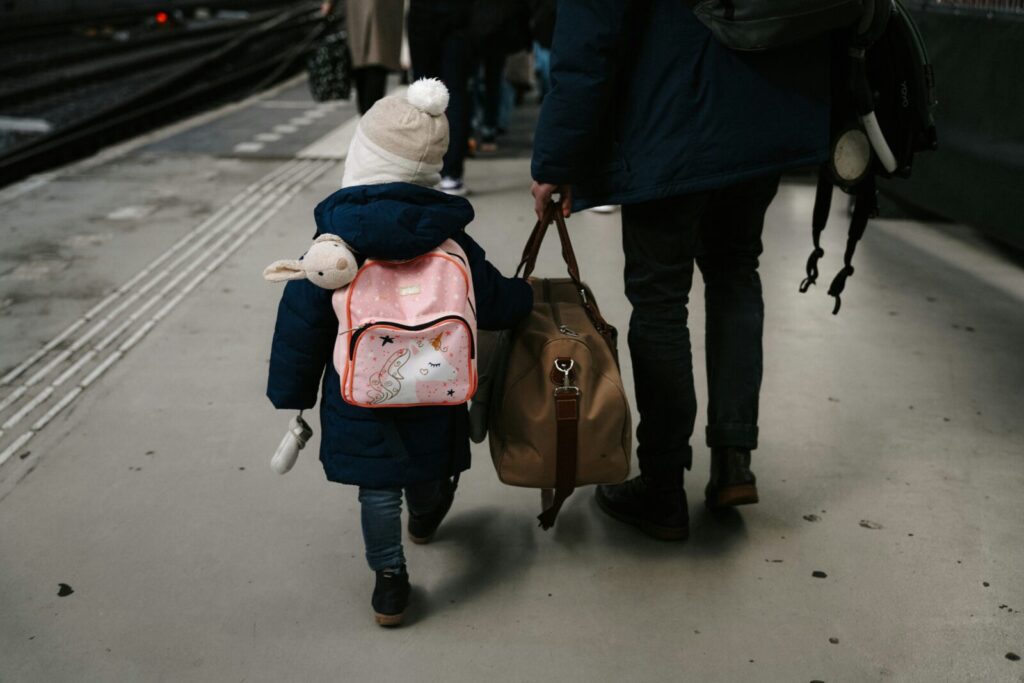 ユニコーンのピンクのリュックを背負った小さな子供と大きな荷物を持つ大人の後ろ姿