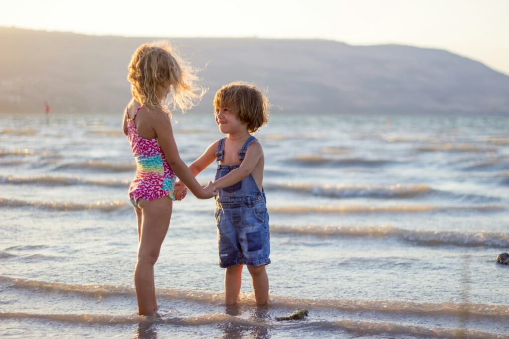 浅瀬で手を繋いで見つめ合う金髪の小さな男の子と少し背の高い女の子