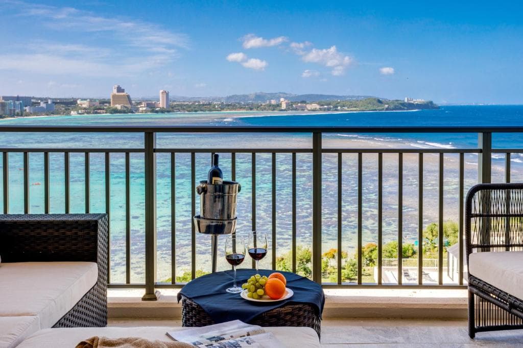ザ ツバキタワーのカメリアルームのバルコニー オーシャンフロントでソファーがあり、フルーツとワイングラスが2つ