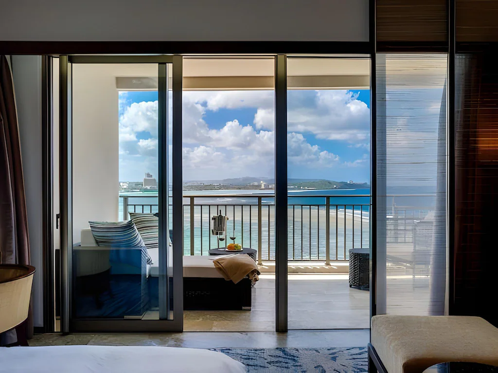 ザ ツバキタワーカメリアルームの客室から大きな窓、ソファーのあるバルコニー、海、空と続いている
