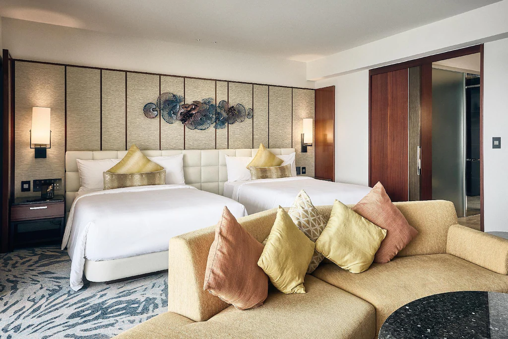 ザ ツバキタワージュニアスイートルーム ダブルサイズベッド2台と広々としたソファー クッションがたくさん並んでいる